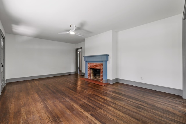 unfurnished living room featuring a brick fireplace, ceiling fan, baseboards, and dark wood-style flooring