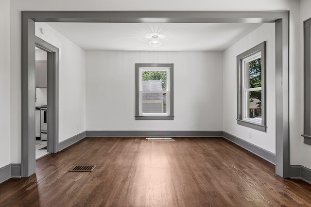 unfurnished room featuring dark wood-style flooring, visible vents, and baseboards