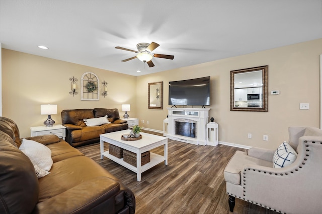 living area featuring baseboards, a fireplace with raised hearth, ceiling fan, dark wood-style flooring, and recessed lighting