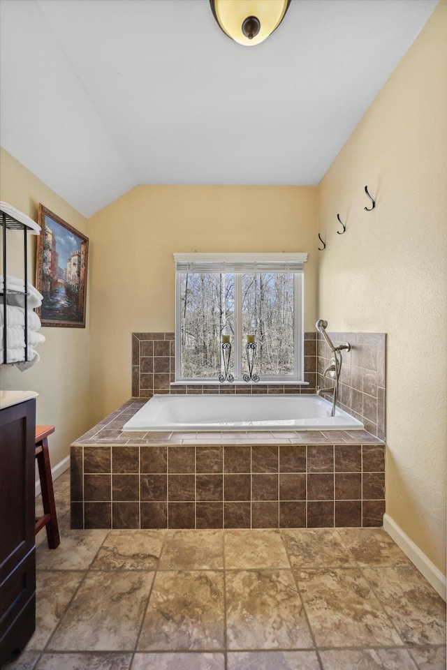 full bathroom featuring vaulted ceiling, a bath, and baseboards