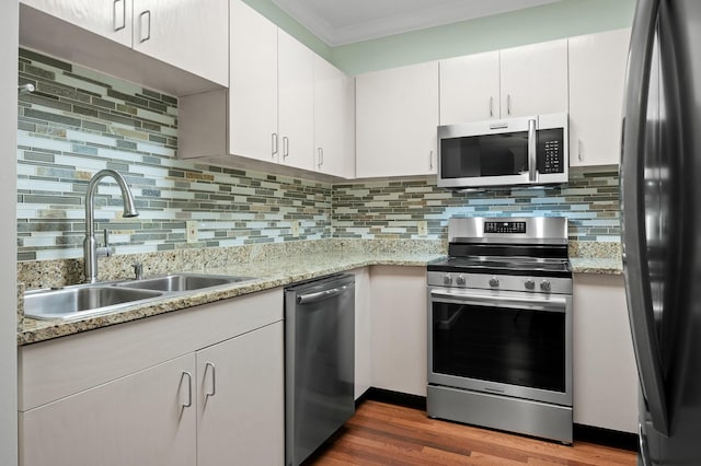 kitchen with tasteful backsplash, ornamental molding, stainless steel appliances, white cabinetry, and a sink