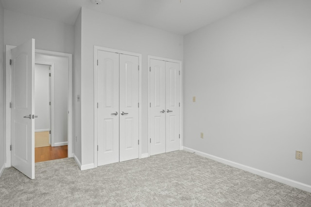 unfurnished bedroom with baseboards, carpet floors, and multiple closets