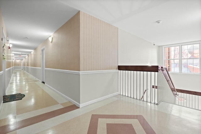 hallway featuring wallpapered walls, tile patterned flooring, baseboards, and an upstairs landing