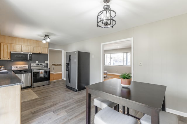 kitchen featuring light wood-style flooring, light brown cabinets, dark countertops, stainless steel appliances, and an inviting chandelier