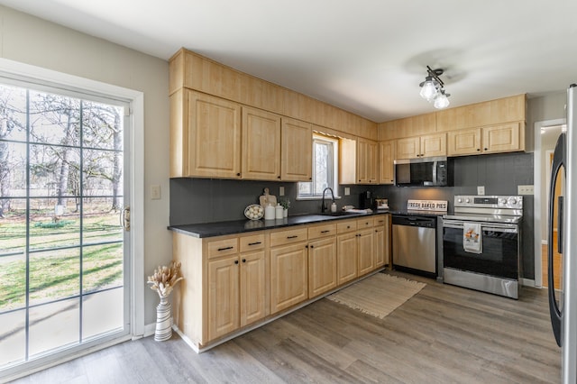 kitchen featuring dark countertops, appliances with stainless steel finishes, wood finished floors, and light brown cabinetry