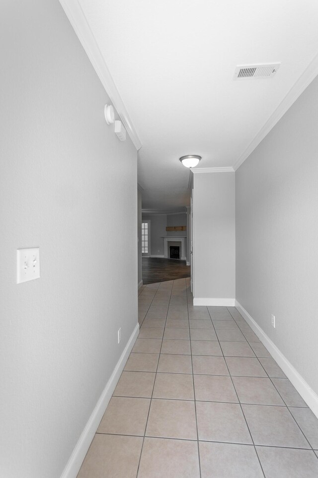 hallway with light tile patterned floors, baseboards, visible vents, and ornamental molding