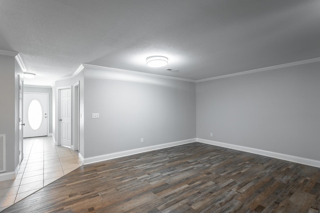 empty room featuring visible vents, dark wood-type flooring, baseboards, ornamental molding, and a textured ceiling