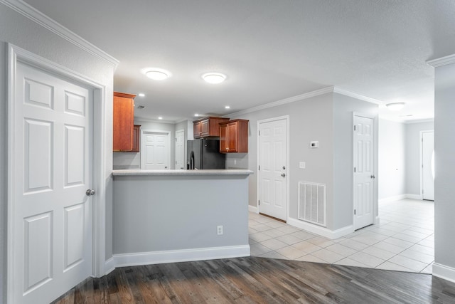 kitchen with visible vents, ornamental molding, black fridge with ice dispenser, wood finished floors, and a peninsula