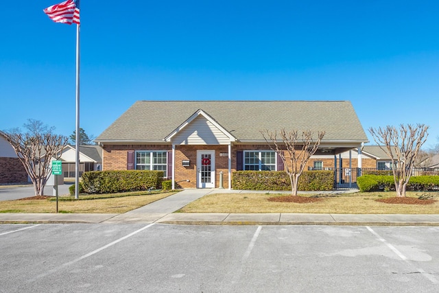 view of front of house featuring a shingled roof, fence, brick siding, and uncovered parking