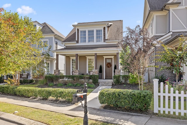 view of front of home with covered porch, a shingled roof, and fence