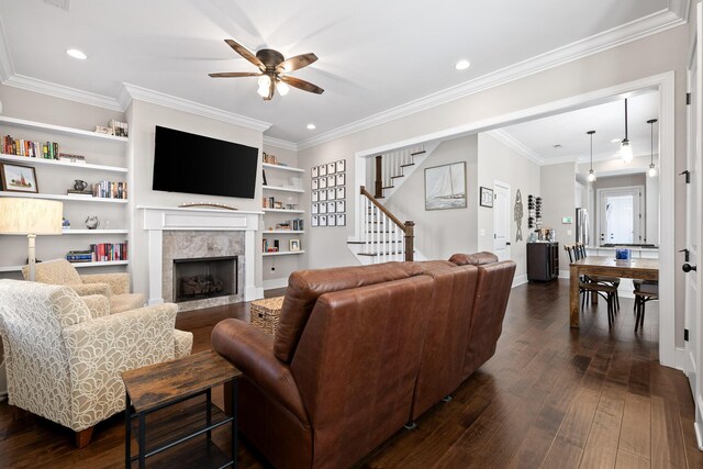 living area with a ceiling fan, a tile fireplace, stairway, ornamental molding, and dark wood-style flooring