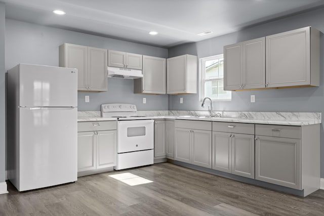 kitchen with white appliances, wood finished floors, under cabinet range hood, a sink, and recessed lighting