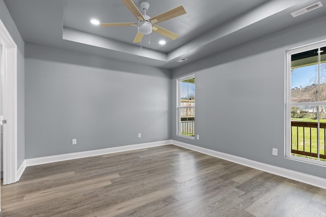 spare room with baseboards, visible vents, a raised ceiling, wood finished floors, and recessed lighting