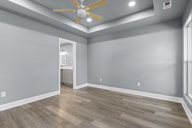 unfurnished bedroom featuring a tray ceiling, recessed lighting, visible vents, wood finished floors, and baseboards