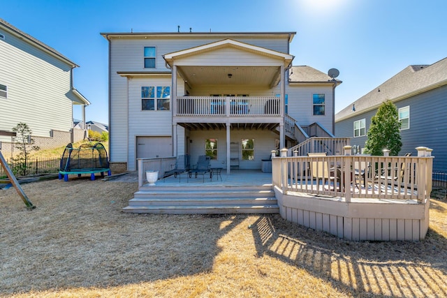 back of house featuring a deck, an attached garage, a trampoline, and fence