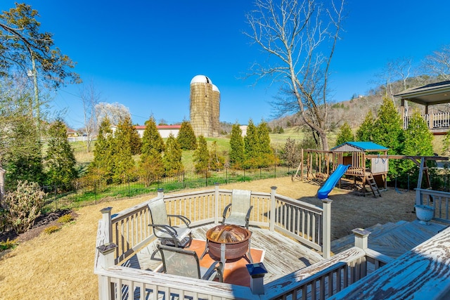 deck with a playground, fence, and an outdoor fire pit