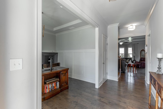 hall with visible vents, crown molding, a wainscoted wall, a decorative wall, and dark wood-style flooring