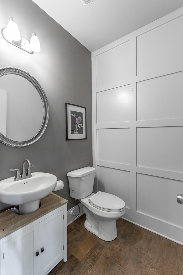 bathroom featuring baseboards, toilet, wood finished floors, and vanity