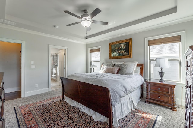 bedroom featuring visible vents, a ceiling fan, ensuite bathroom, a tray ceiling, and baseboards