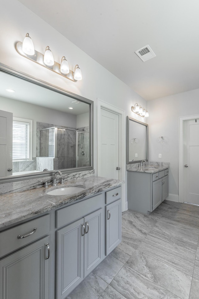 full bath with a shower stall, two vanities, visible vents, and a sink