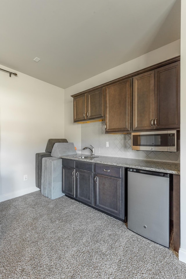 kitchen featuring a sink, stainless steel microwave, fridge, dark brown cabinetry, and decorative backsplash