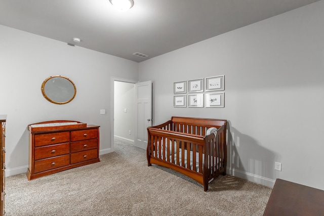 bedroom with visible vents, a crib, baseboards, and carpet