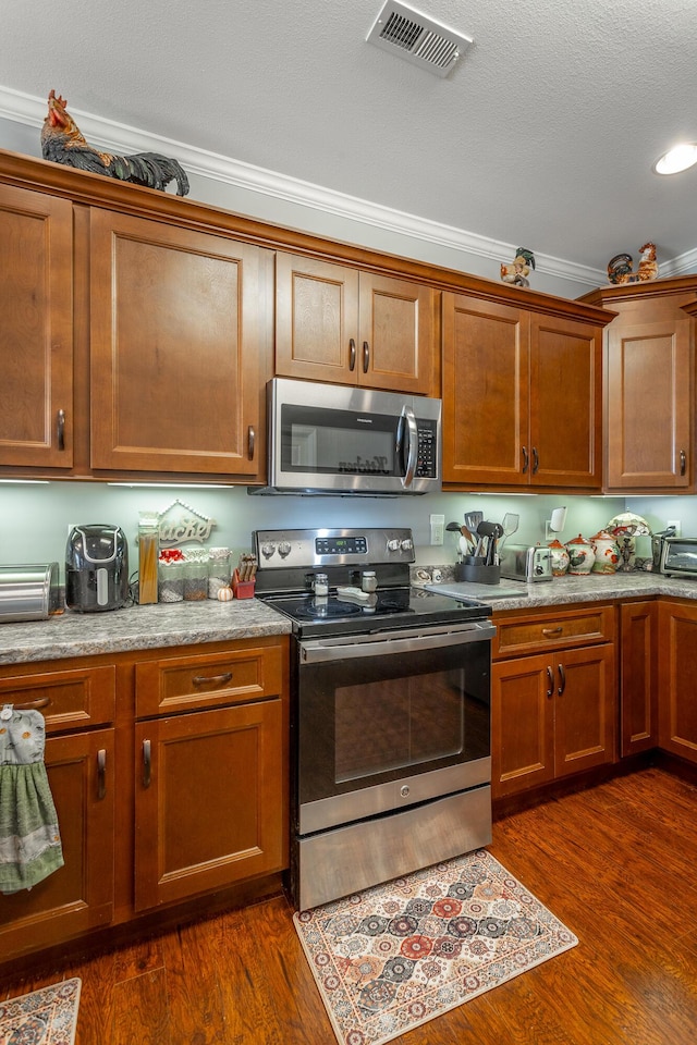 kitchen featuring dark wood-style floors, brown cabinets, stainless steel appliances, visible vents, and ornamental molding