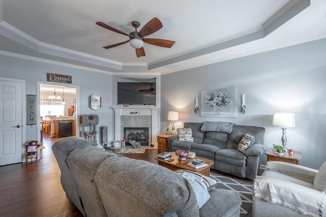 living area featuring a raised ceiling, a tile fireplace, ornamental molding, wood finished floors, and ceiling fan with notable chandelier