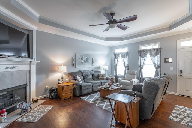 living area with ornamental molding, a raised ceiling, a tiled fireplace, and hardwood / wood-style flooring