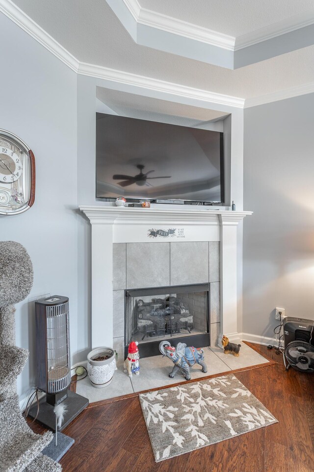 interior details featuring wood finished floors, a tile fireplace, a ceiling fan, and crown molding