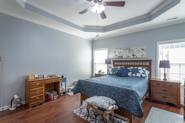 bedroom with a tray ceiling, wood finished floors, and visible vents