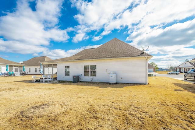 rear view of property with central air condition unit, a sunroom, and a shingled roof