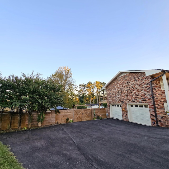 view of side of property with a garage, aphalt driveway, a gate, fence, and brick siding