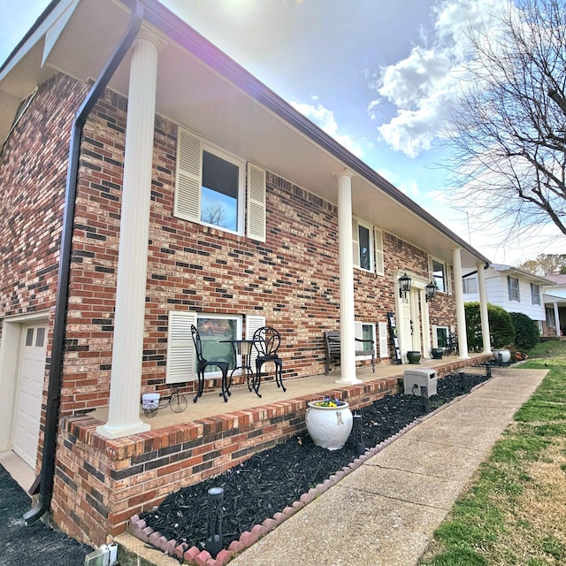 view of side of property with covered porch, brick siding, and an attached garage