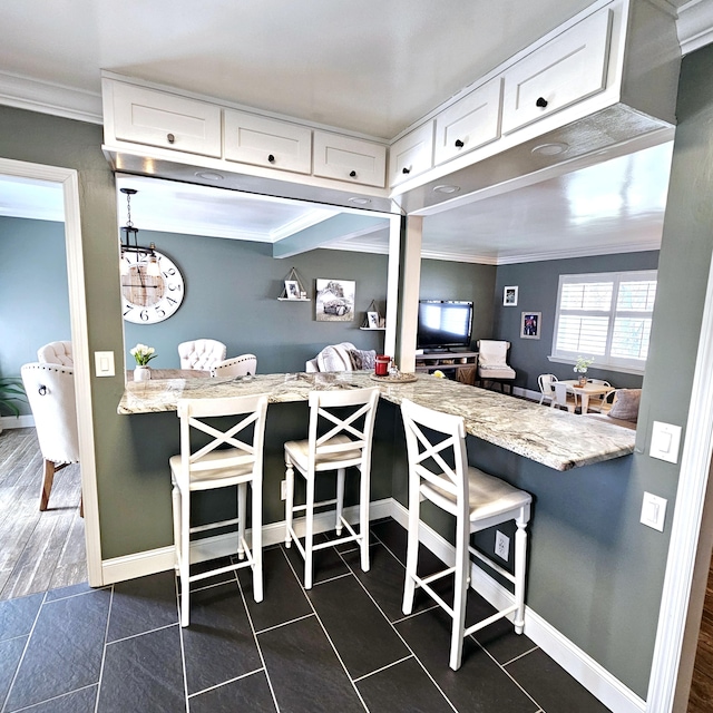 kitchen with a breakfast bar area, ornamental molding, white cabinetry, dark tile patterned flooring, and baseboards