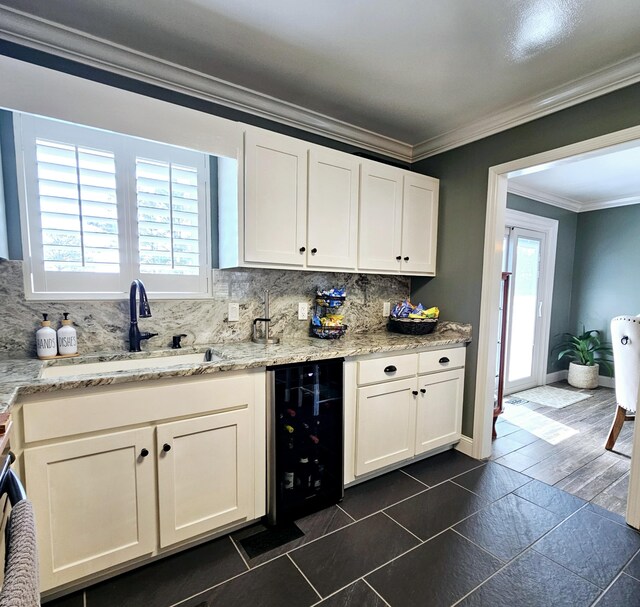 kitchen featuring beverage cooler, a sink, white cabinetry, backsplash, and crown molding