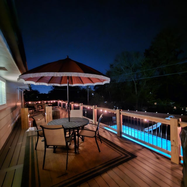 deck at twilight with outdoor dining space and an outdoor pool