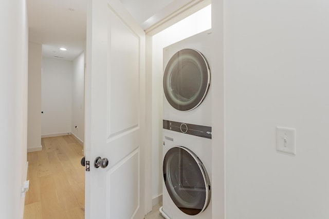 laundry area featuring stacked washer and dryer, laundry area, baseboards, and light wood finished floors