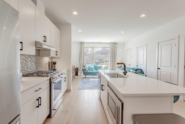 kitchen with light wood finished floors, open floor plan, stainless steel appliances, under cabinet range hood, and a sink