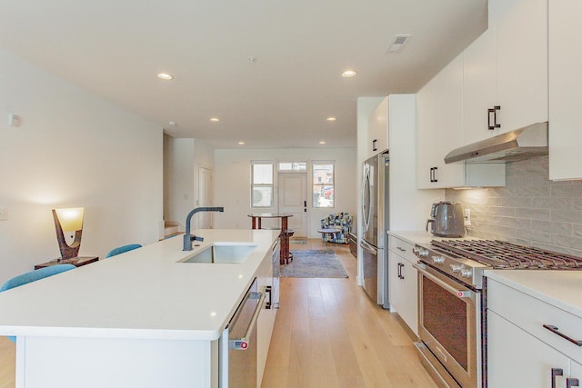 kitchen with light wood-style flooring, decorative backsplash, appliances with stainless steel finishes, a sink, and under cabinet range hood