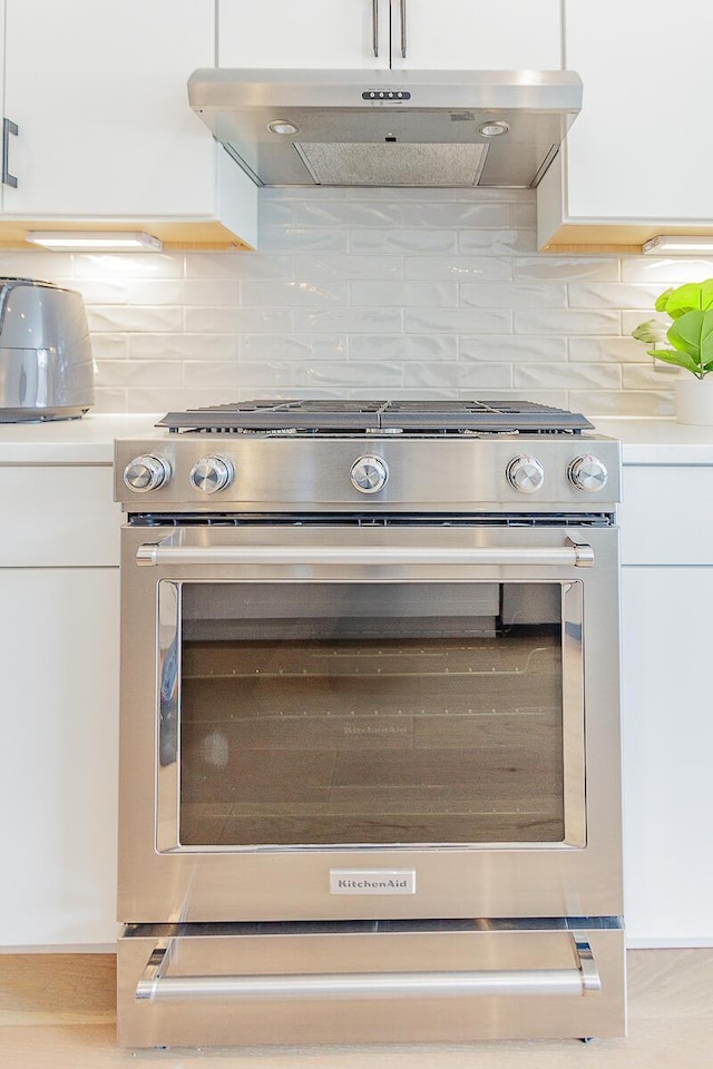 kitchen with gas stove, white cabinetry, and under cabinet range hood