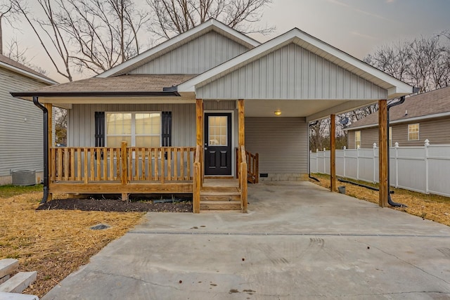 view of front of home featuring roof with shingles, a porch, concrete driveway, fence, and a carport