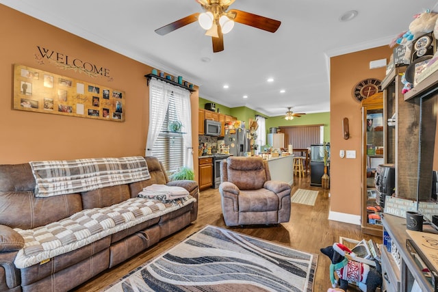 living room featuring ceiling fan, recessed lighting, baseboards, light wood finished floors, and crown molding