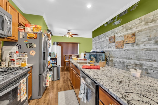 kitchen featuring stainless steel appliances, brown cabinets, crown molding, and light wood finished floors