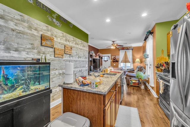 kitchen with stainless steel appliances, a sink, open floor plan, brown cabinets, and crown molding