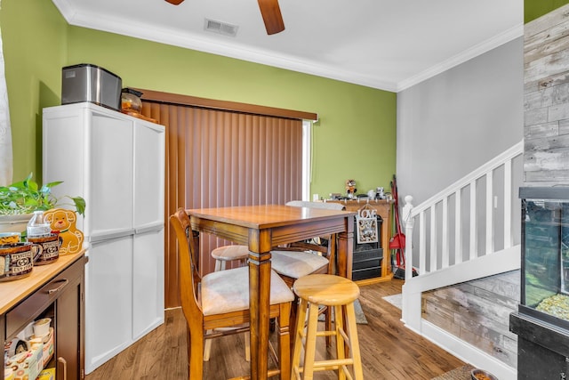 dining room featuring ceiling fan, visible vents, stairs, ornamental molding, and light wood finished floors