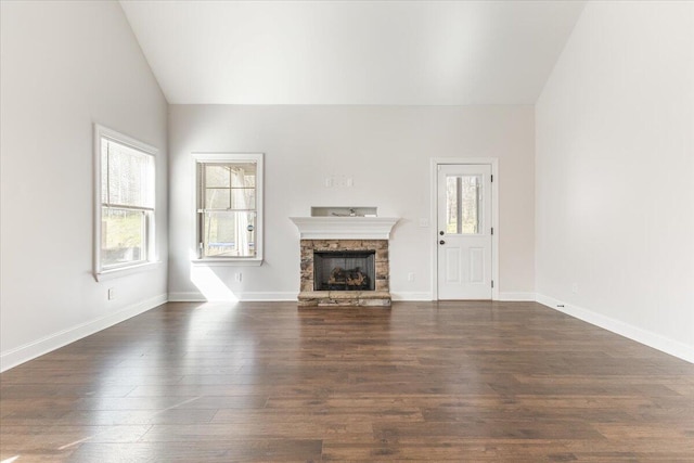 unfurnished living room with a stone fireplace, dark wood-type flooring, plenty of natural light, and vaulted ceiling