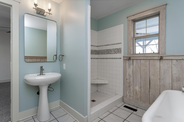 full bathroom featuring wooden walls, baseboards, a tile shower, a sink, and tile patterned floors