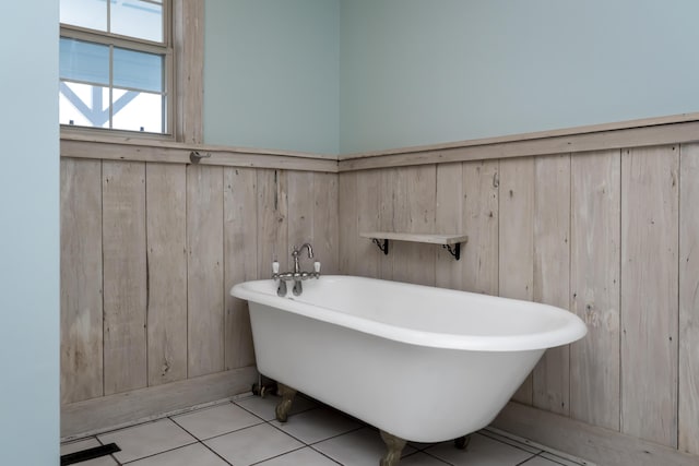 bathroom featuring tile patterned floors, wooden walls, and a freestanding bath