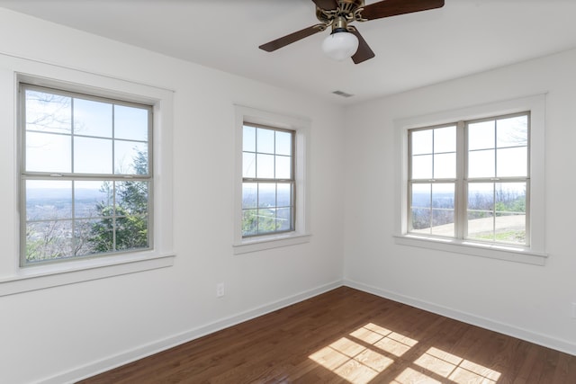 unfurnished room with visible vents, a healthy amount of sunlight, dark wood-type flooring, and baseboards